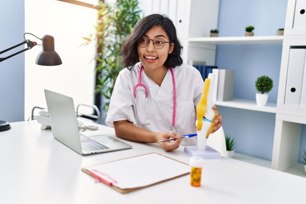 A student taking Online Courses for Health, studying with a book on the table while focusing on her laptop and listening attentively