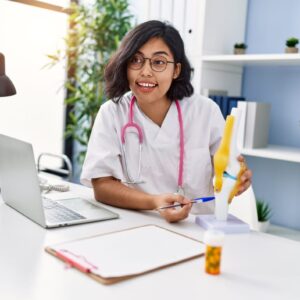 A student taking Online Courses for Health, studying with a book on the table while focusing on her laptop and listening attentively