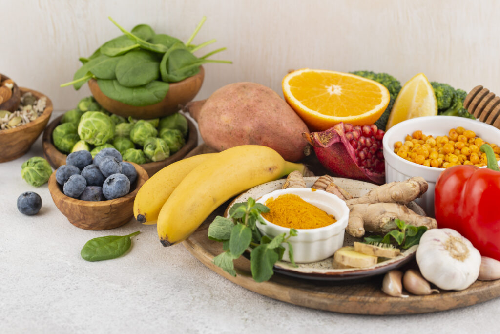 An assortment of foods that boost your immune system naturally, including citrus fruits, spinach, blueberries, ginger, garlic, turmeric, yogurt, and fresh vegetables, on a wooden table.