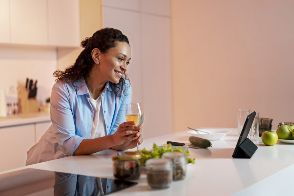 Daily preventive health tip concept: a woman drinks water and prepares healthy food in a bright kitchen, following a balanced wellness routine.