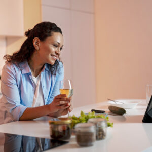 Daily preventive health tip concept: a woman drinks water and prepares healthy food in a bright kitchen, following a balanced wellness routine.